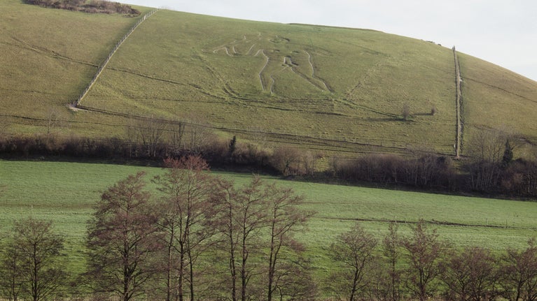 View of Cerne Abbas chalk giant on hill beyond autumnal trees in Dorset.